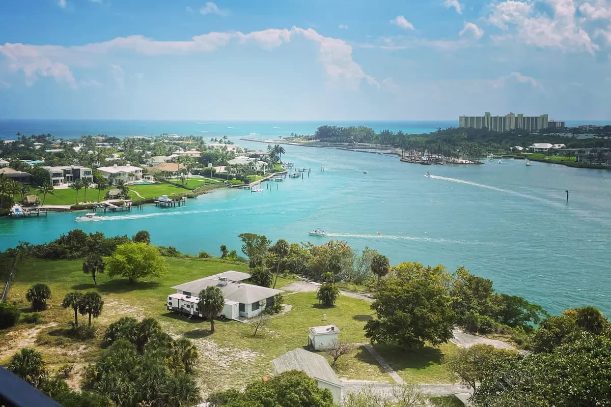The Jupiter Inlet seen from the top of the Jupiter Inlet Lighthouse, with houses and docks on the north bank at left, boats on turquoise water, the Atlantic beyond, and condominium towers south of the inlet on the right