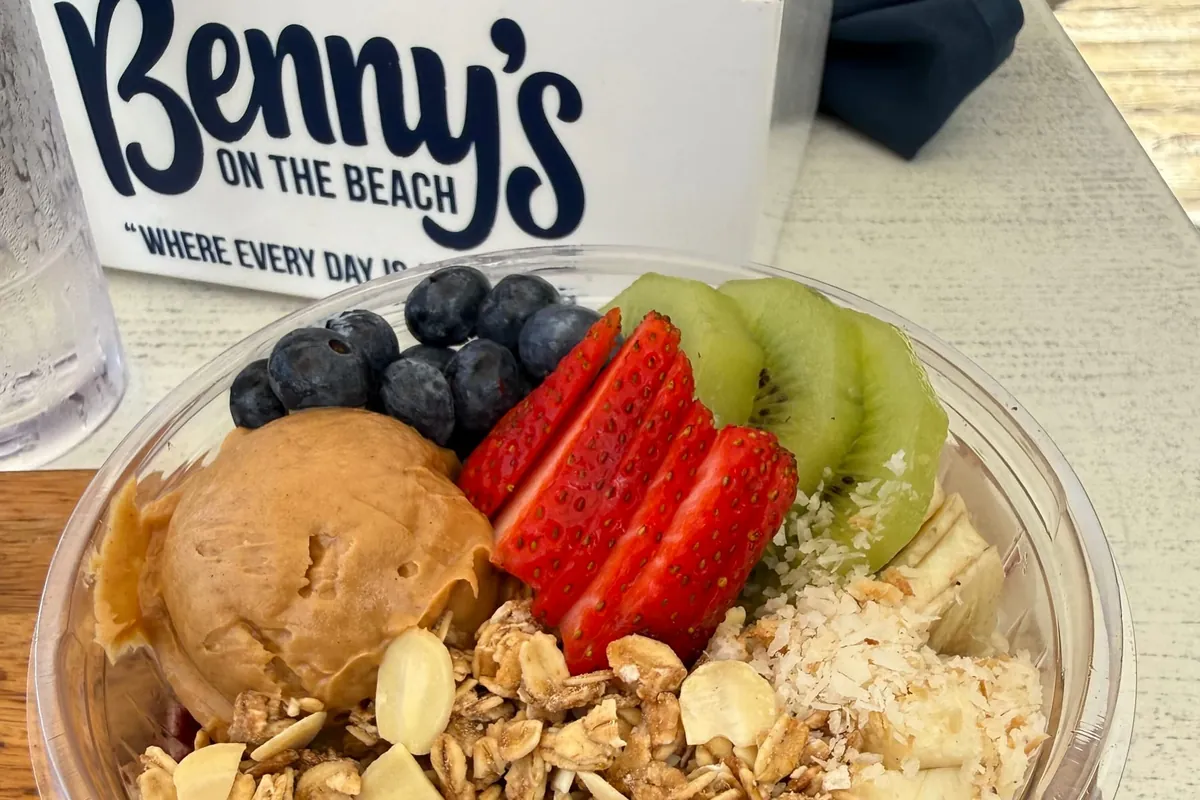 An açaí bowl topped with blueberries, strawberries, kiwi, granola and a scoop of nut butter on a table at Benny's on the Beach, the restaurant at the Lake Worth Beach pier, with the Benny's table card behind it