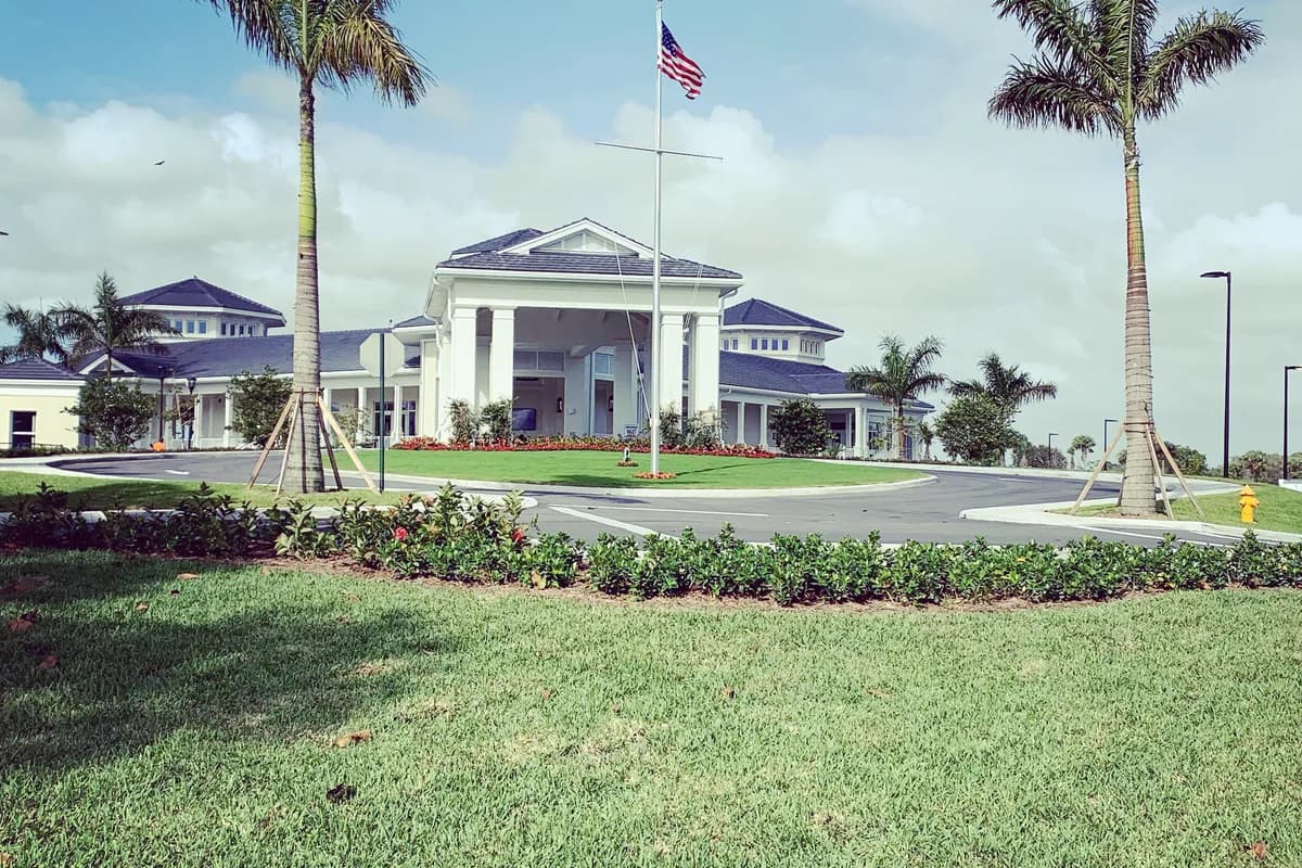 A white clubhouse with a columned entrance and a blue roof behind a lawn and landscaped drive