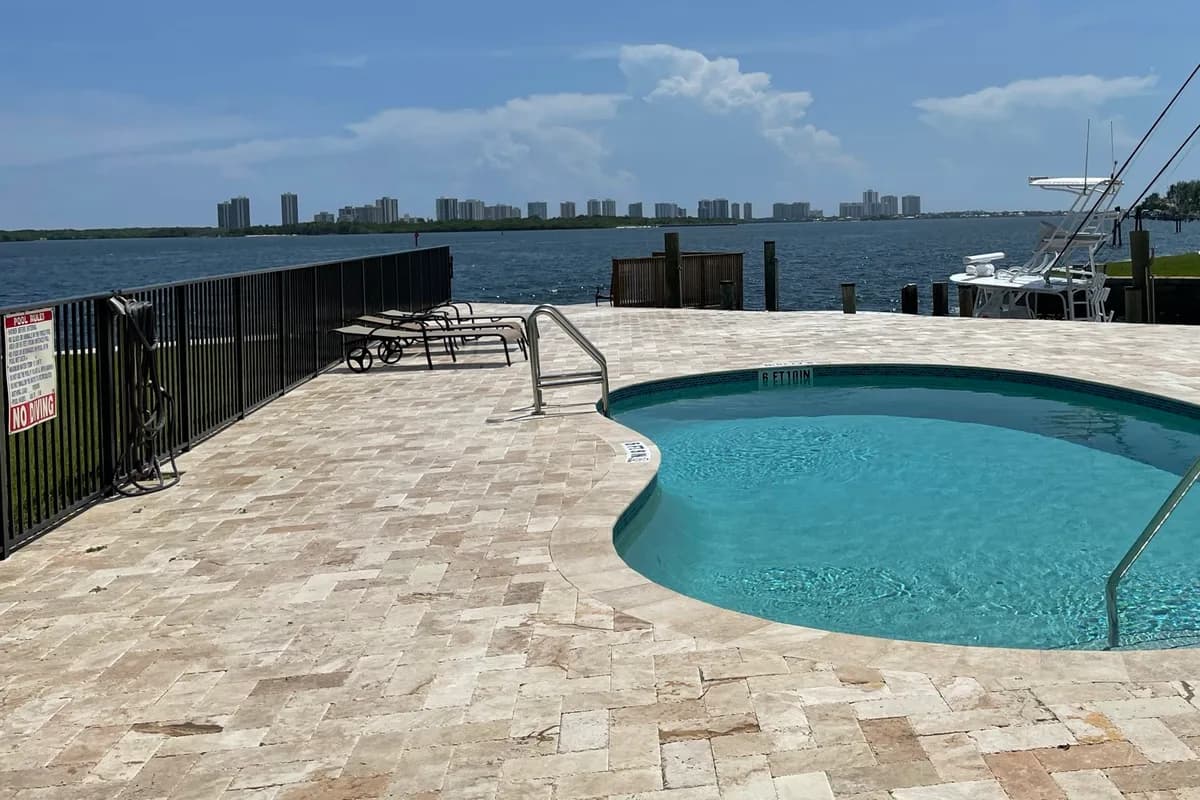 A waterfront terrace overlooking a wide waterway with a distant shoreline of high-rise buildings under a blue sky