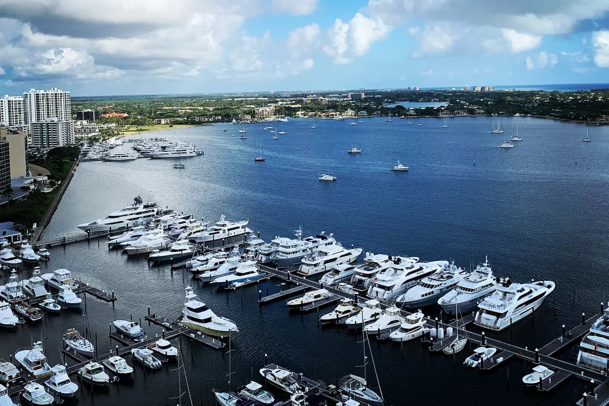 An elevated view of a marina with moored yachts along the docks and a wide waterway under a blue sky
