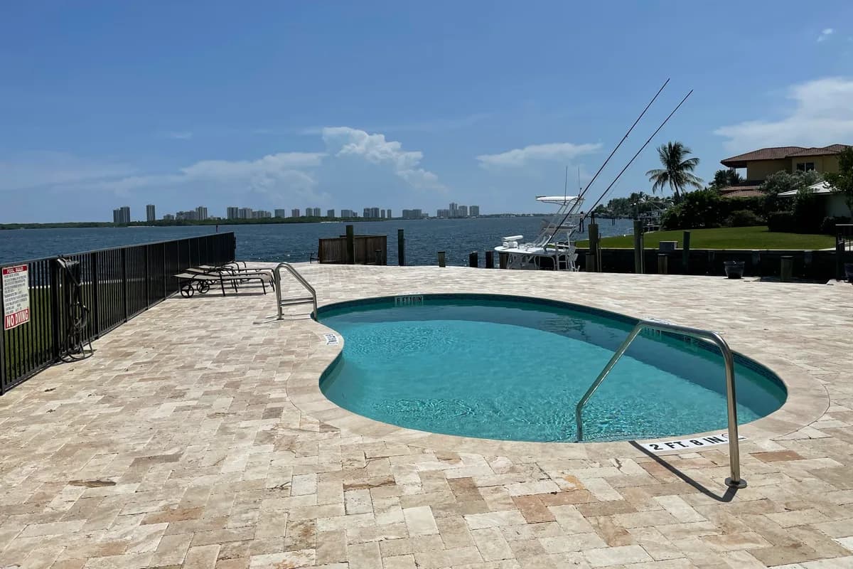 A waterfront pool deck beside a wide waterway with a distant skyline