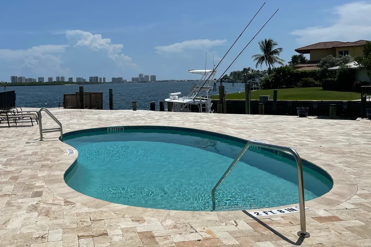 A pool and dock beside a waterway with a sport-fishing boat and a waterfront house