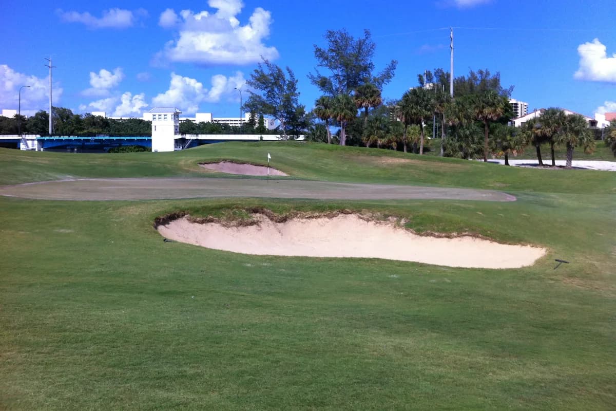 A golf green and sand bunker with a drawbridge tower and palms behind