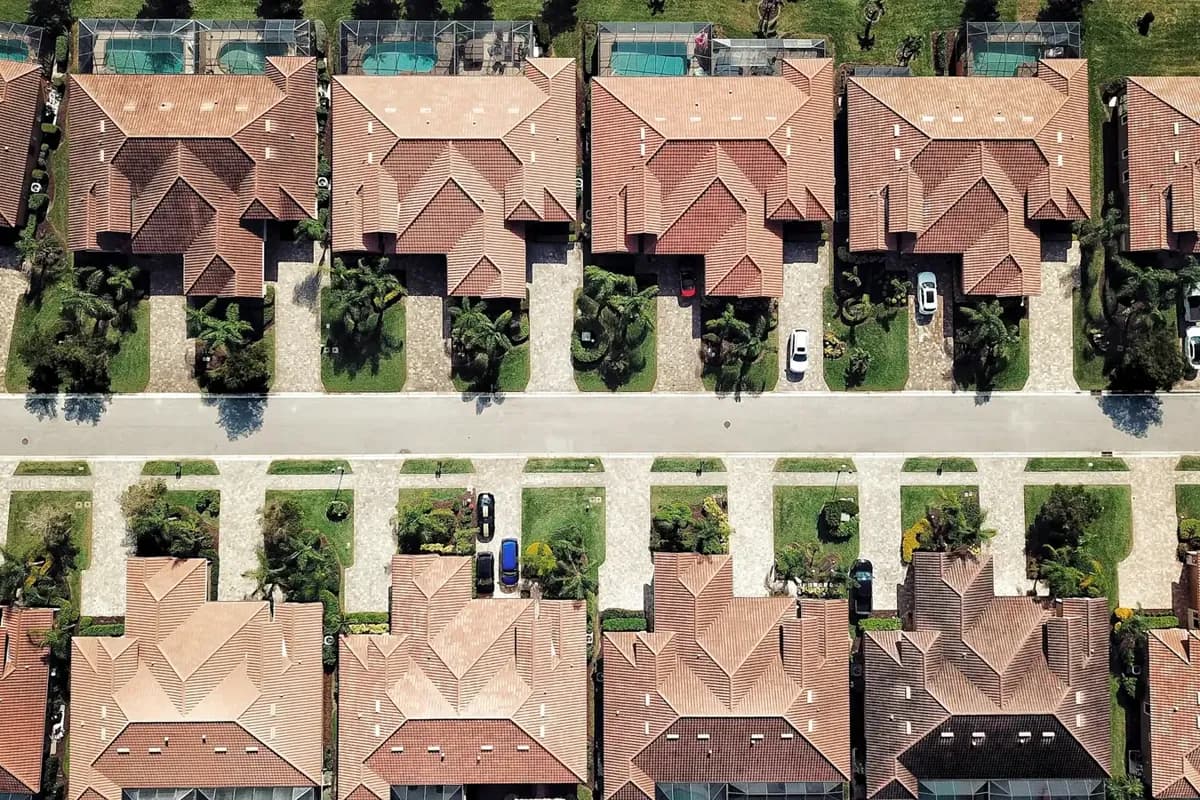 A top-down drone view of rows of tile-roof single-family houses with pool cages and driveways along a street grid