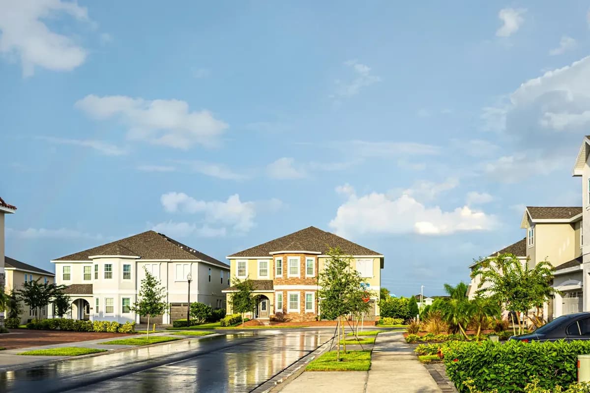 A rain-wet suburban street with pastel two-story homes, hedges and a bright sky
