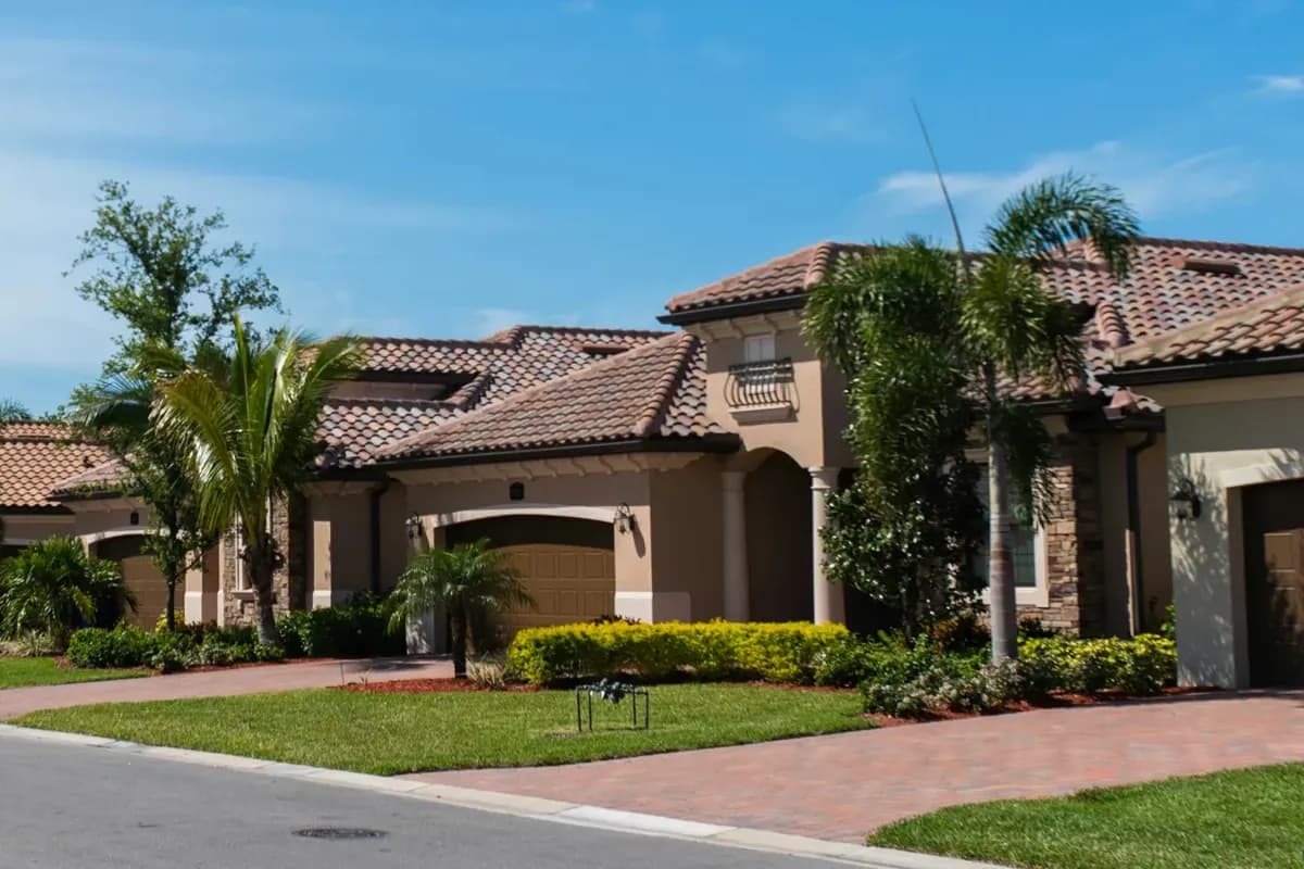 Tile-roof homes with garages, lawns, palm trees and a paver driveway beside a quiet residential street