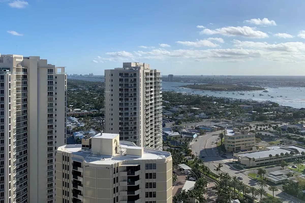 A high view south over Singer Island's condominium towers and house streets to the lagoon, with Peanut Island and boats at anchor beyond