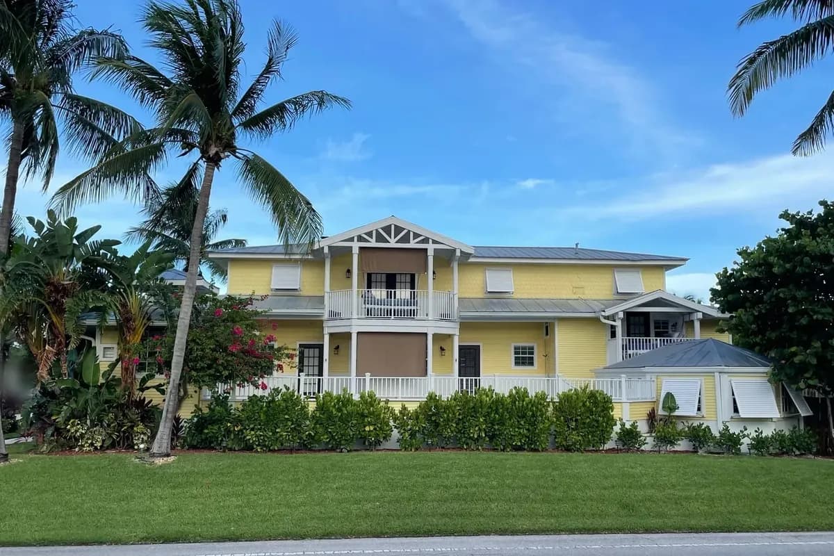 A yellow two-story house with a white porch and palm trees on a Singer Island street