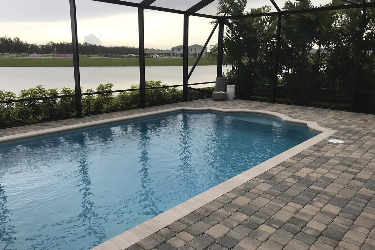 A screened swimming pool on a paver deck at a Minto model home in Westlake, looking across a lake to a few two-story houses, construction equipment and graded land