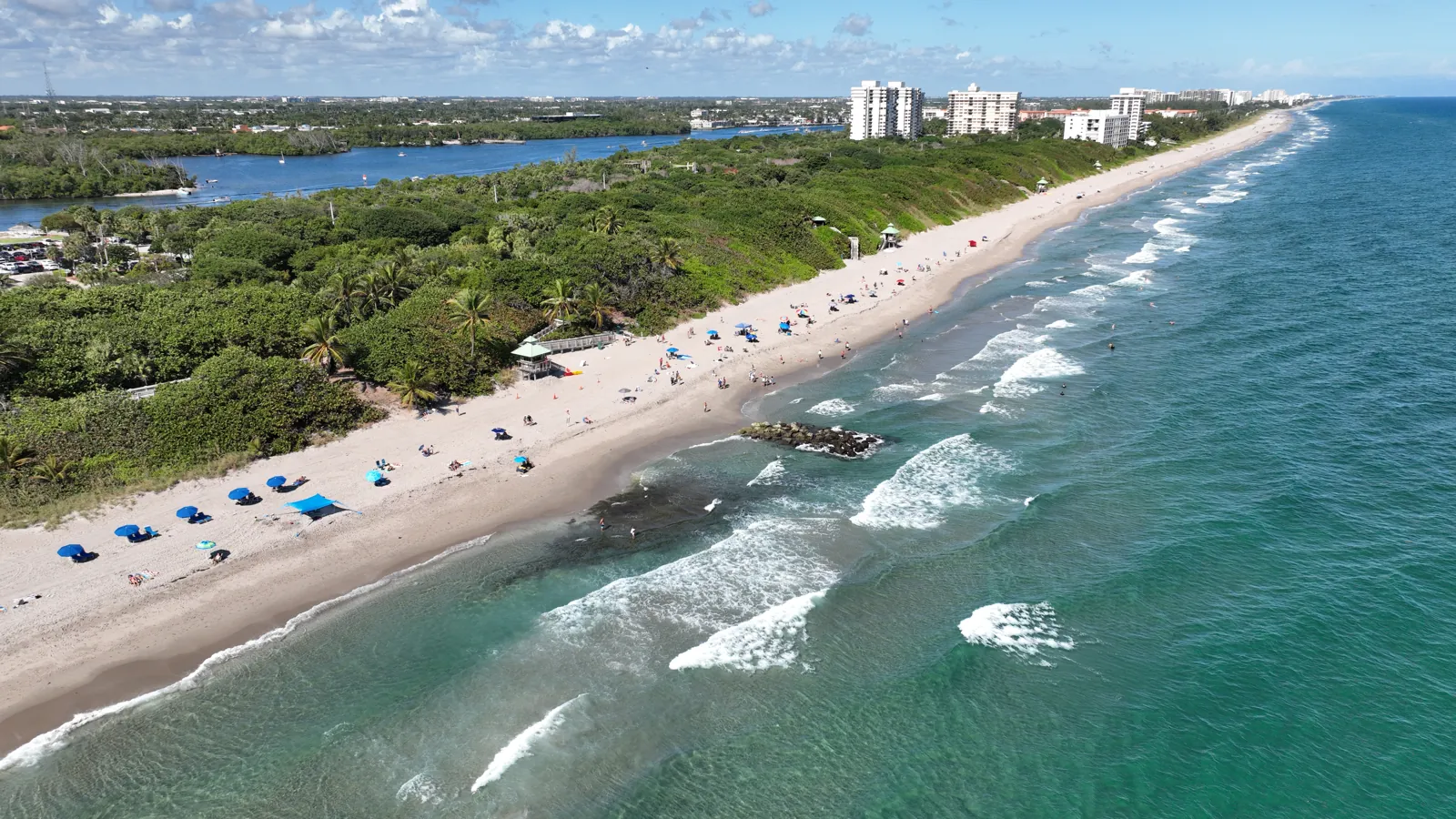 Aerial view of a barrier-island beach with turquoise surf, dune vegetation, and the Intracoastal waterway