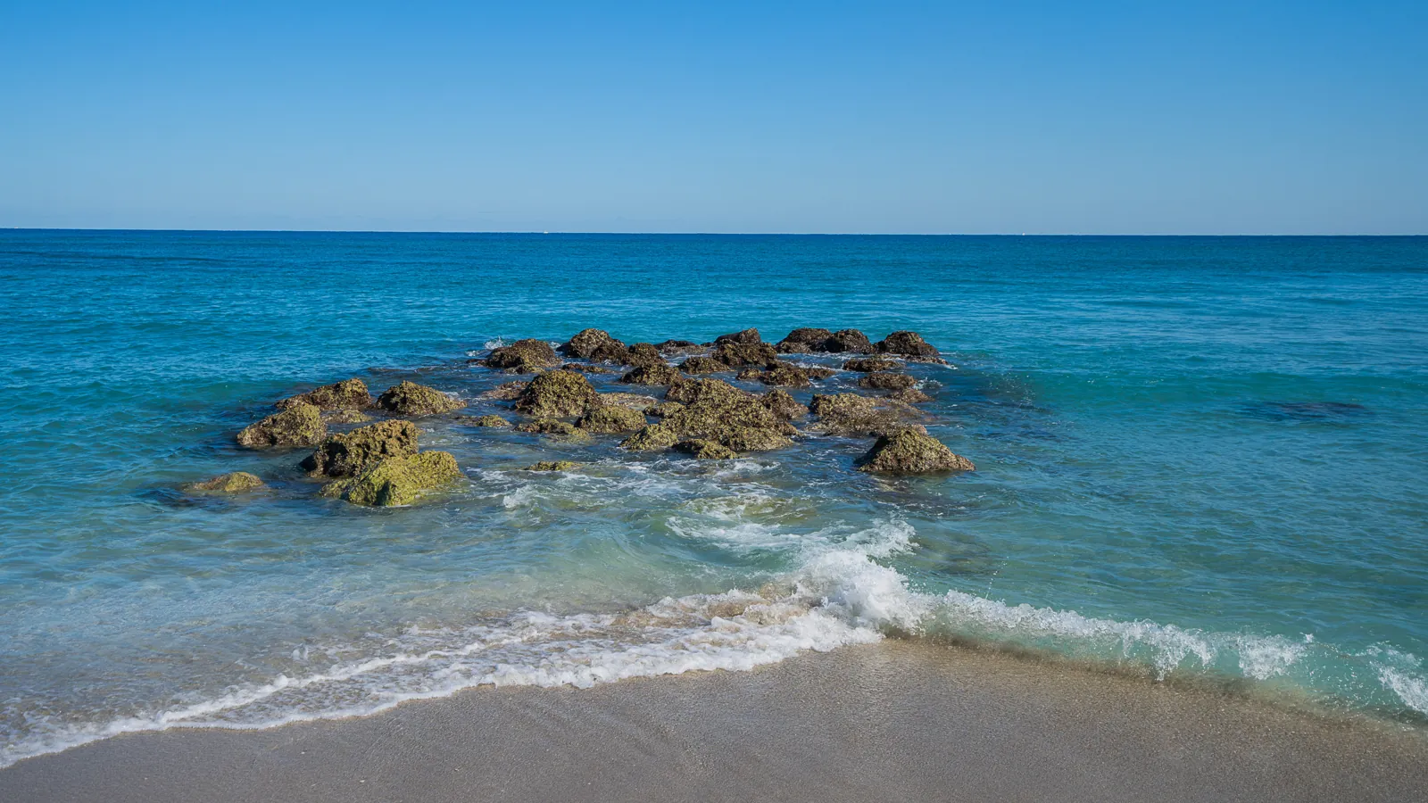 Rocky limestone outcrop in turquoise surf with gentle shore break