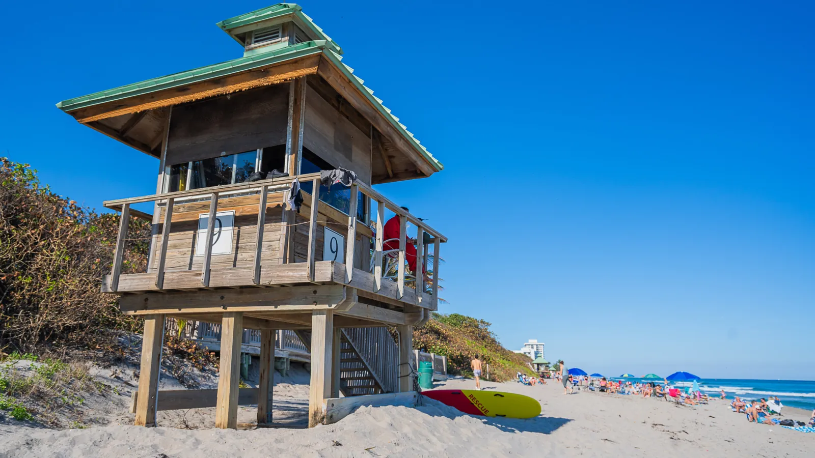 Wooden lifeguard tower #9 on a sandy beach with green metal roof