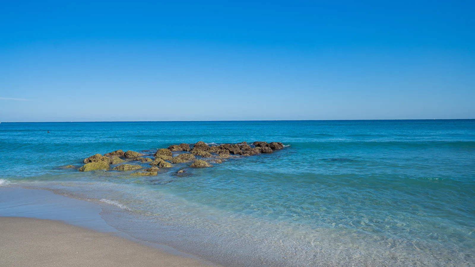 Rocky outcrop in turquoise Atlantic surf with sandy beach foreground