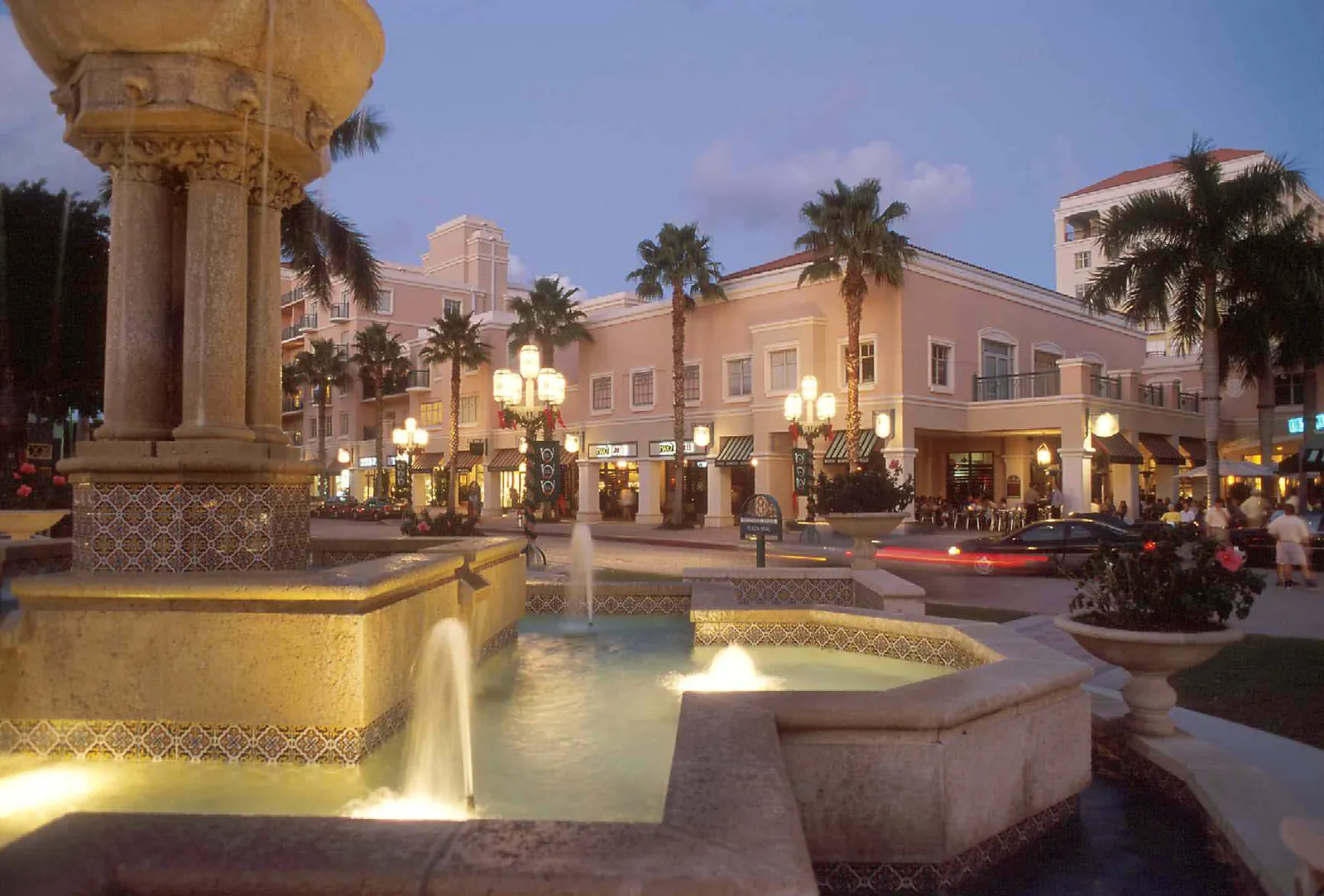 Illuminated stone fountain in a Mediterranean-style outdoor shopping plaza at dusk