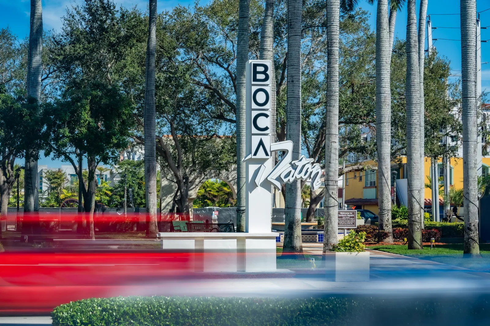 Boca Raton city sign monument framed by royal palms with motion-blurred traffic in foreground
