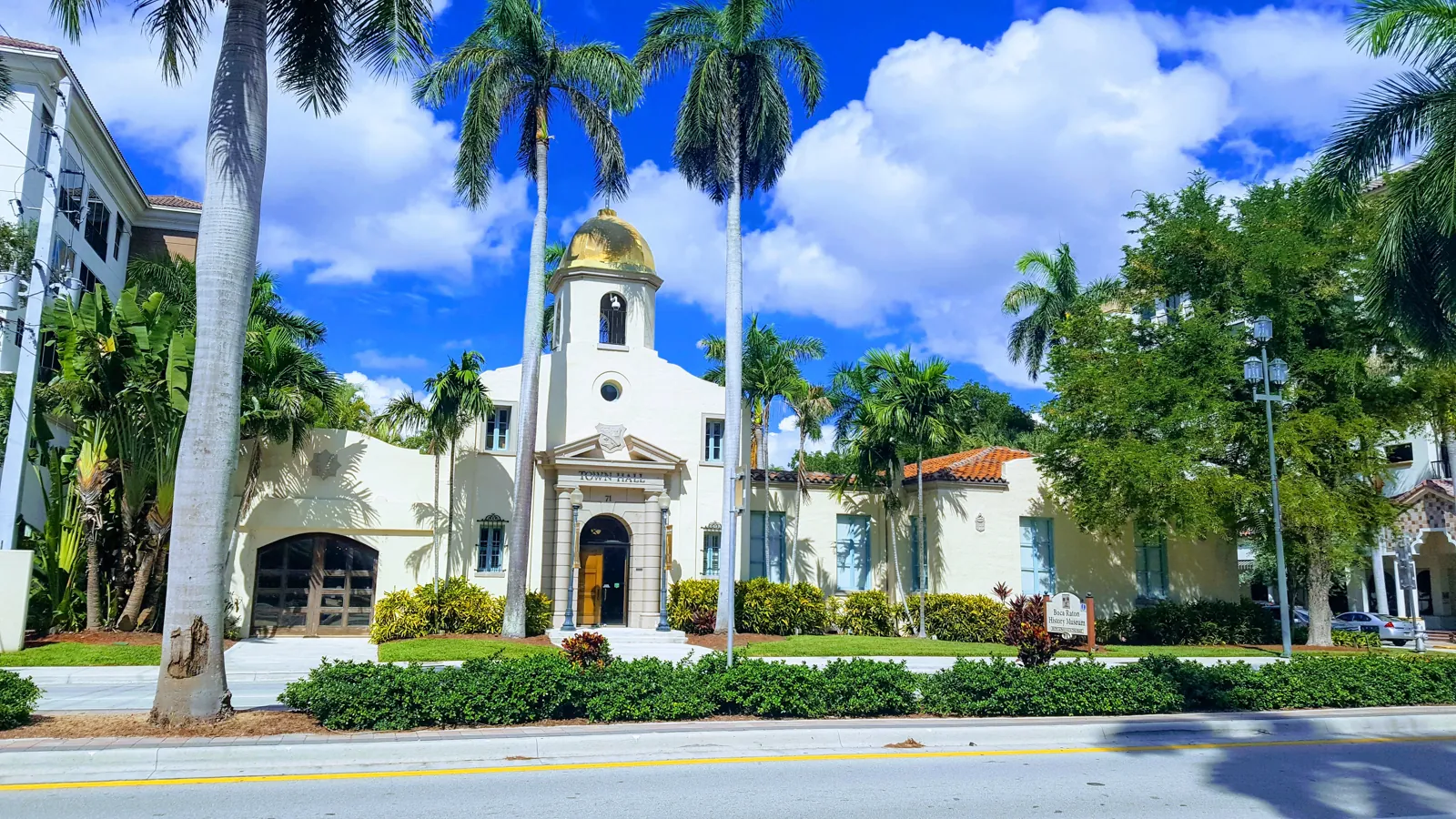Mediterranean Revival civic building with gold dome cupola, framed by royal palms
