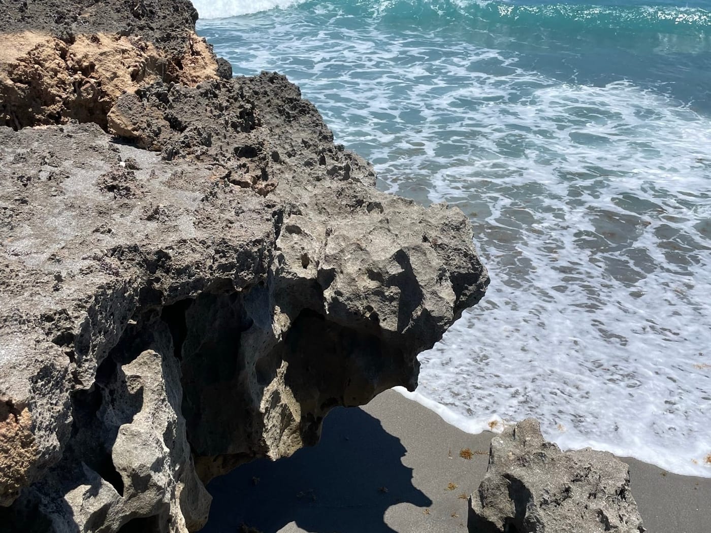 Eroded limestone overhanging the beach as waves break against it at Blowing Rocks Preserve