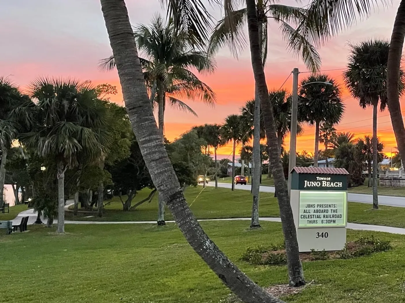 The Town of Juno Beach sign among palms at sunset, its marquee advertising a Celestial Railroad talk