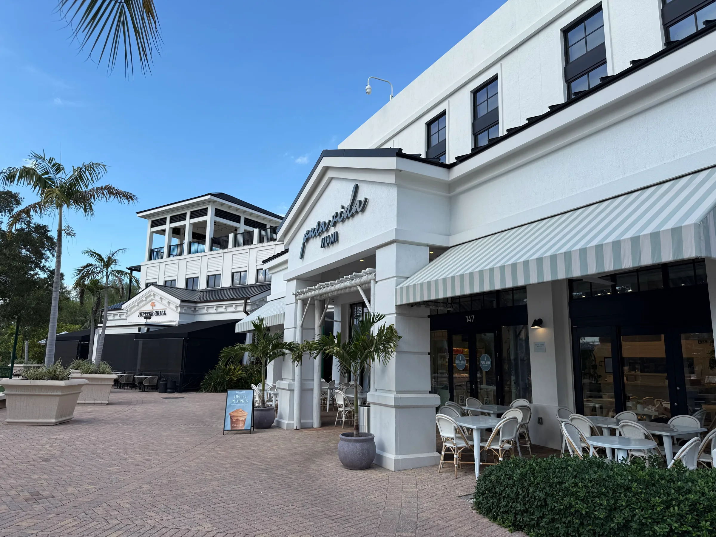 Pura Vida at Harbourside Place, with a striped awning and patio tables, and The Jupiter Grill behind it across the brick plaza