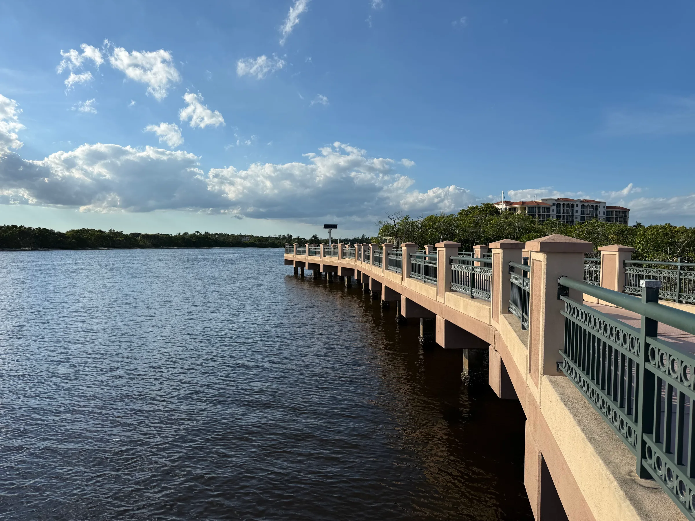 The Riverwalk boardwalk curving out over the Intracoastal on concrete piers, with mangroves and a mid-rise building on the shore