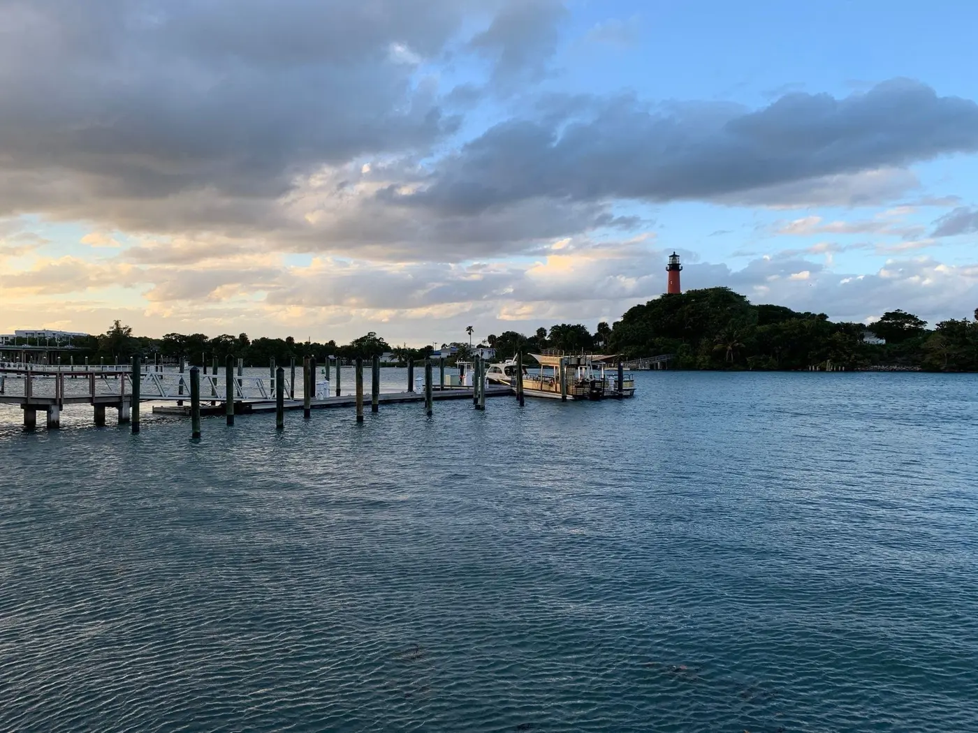 The Jupiter Inlet Lighthouse on its point at dusk, seen across the water past dock pilings