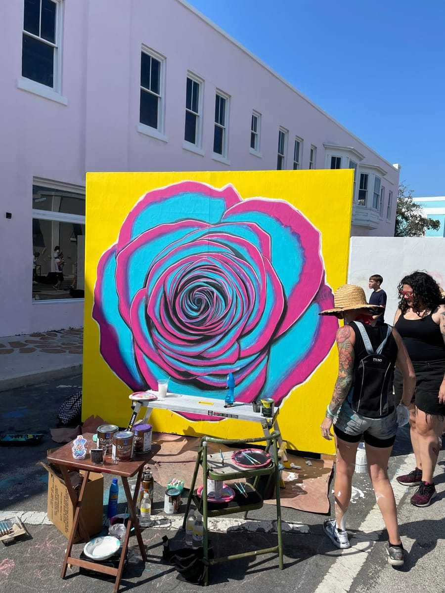 A large pink and cyan rose painted on a panel against a lavender downtown building