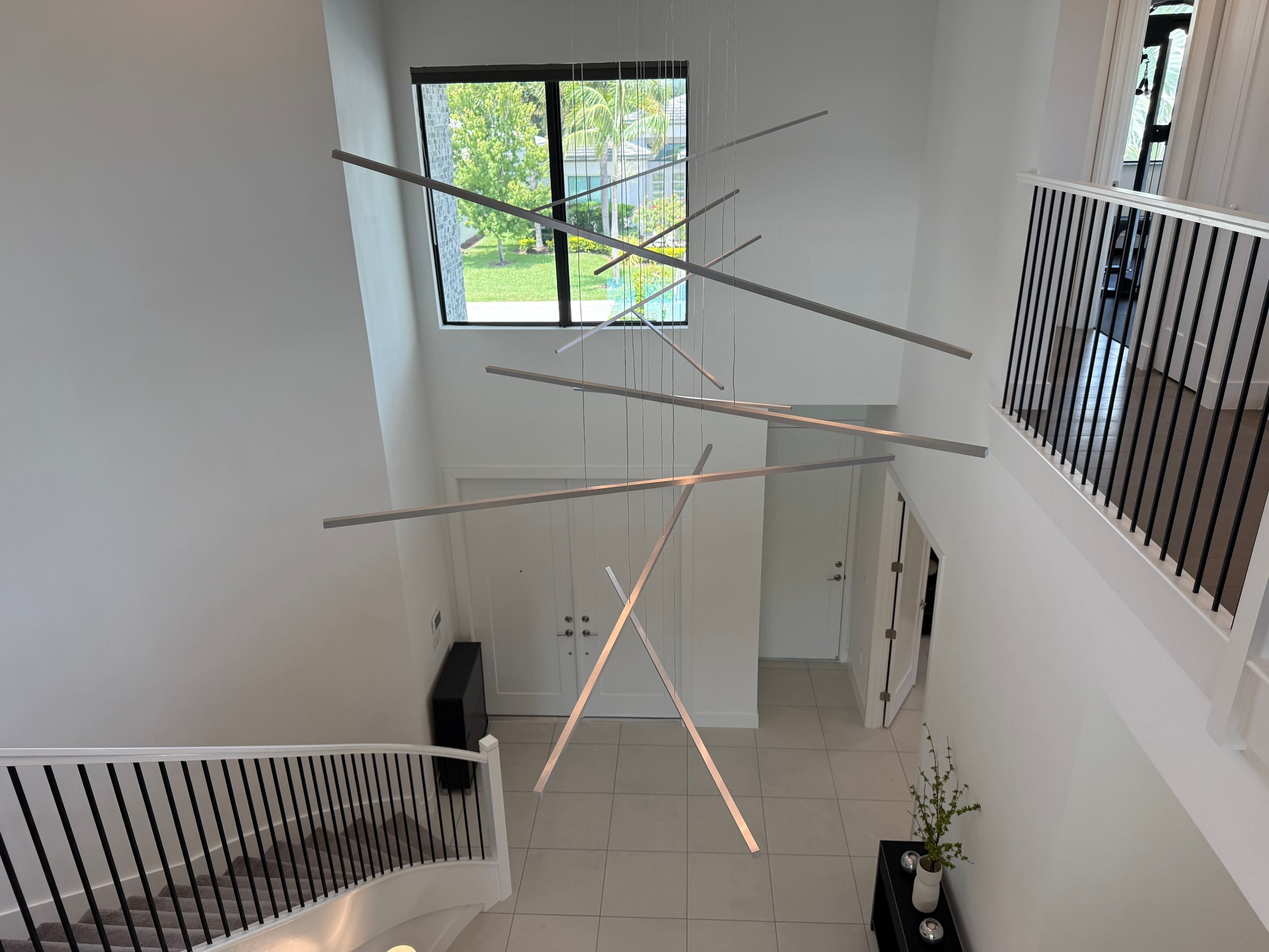 The two-story foyer at 8804 Skyward Street seen from the upstairs loft, with a linear bar chandelier suspended over the entry and a curved staircase below