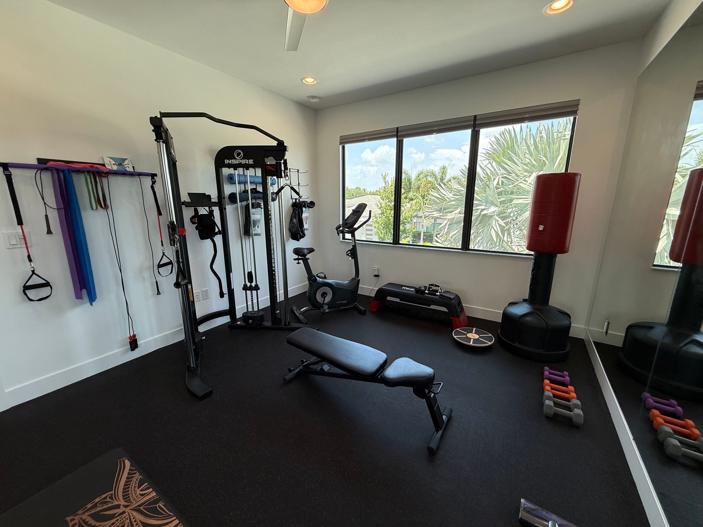 The home gym at 8804 Skyward Street, with a mirrored wall, rubber flooring, a cable machine, bench, exercise bike and heavy bag