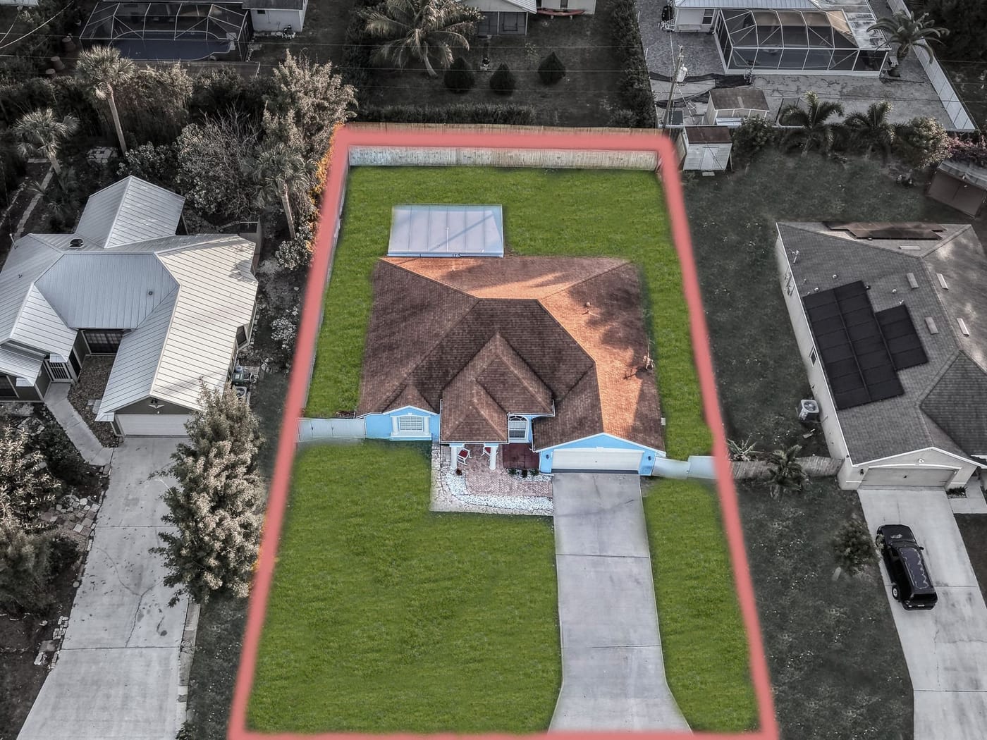 Aerial view of a single-family lot outlined in red, with the house, driveway and fenced backyard between neighboring homes