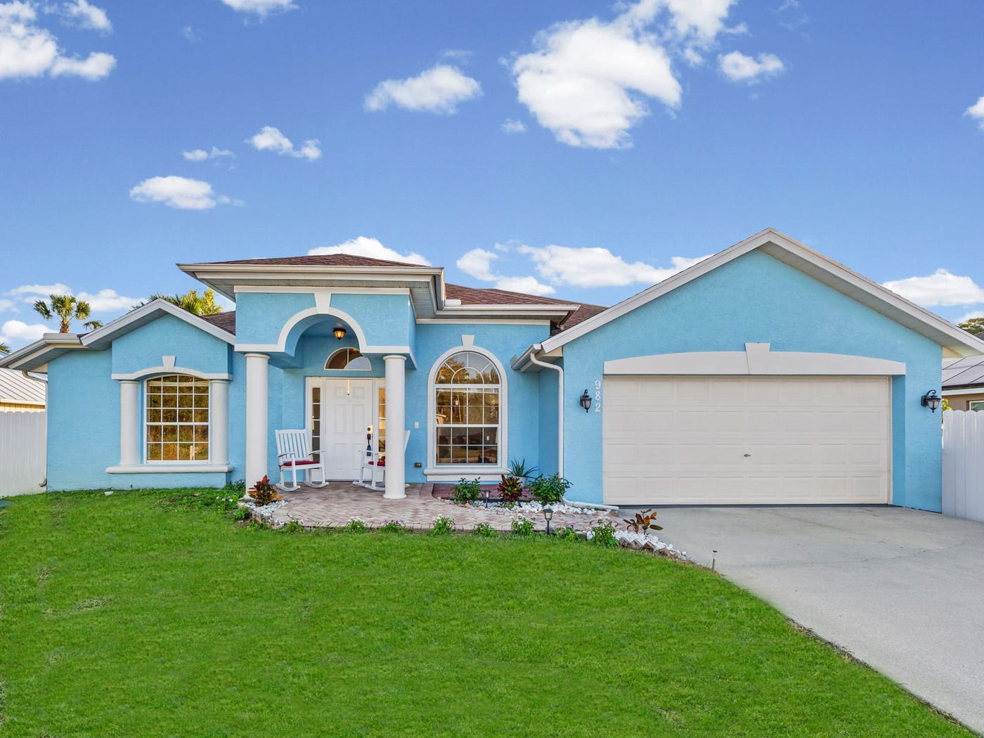 A single-story powder-blue home with a two-car garage and a green front lawn