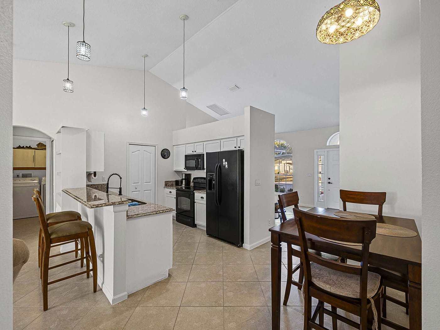A white kitchen with an island, pendant lights and an adjoining dining area