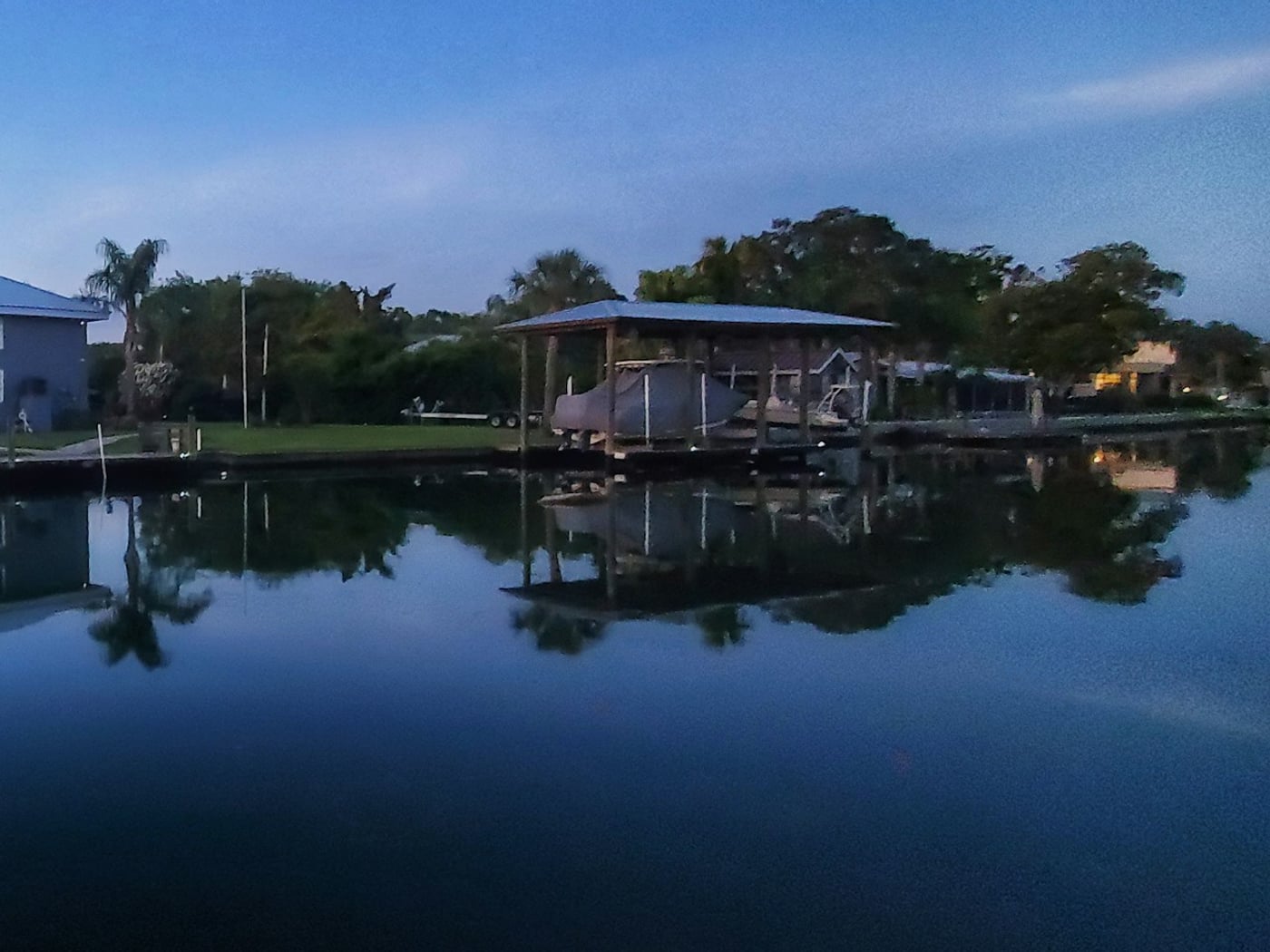 A covered boat lift and dock on a quiet residential canal at dusk