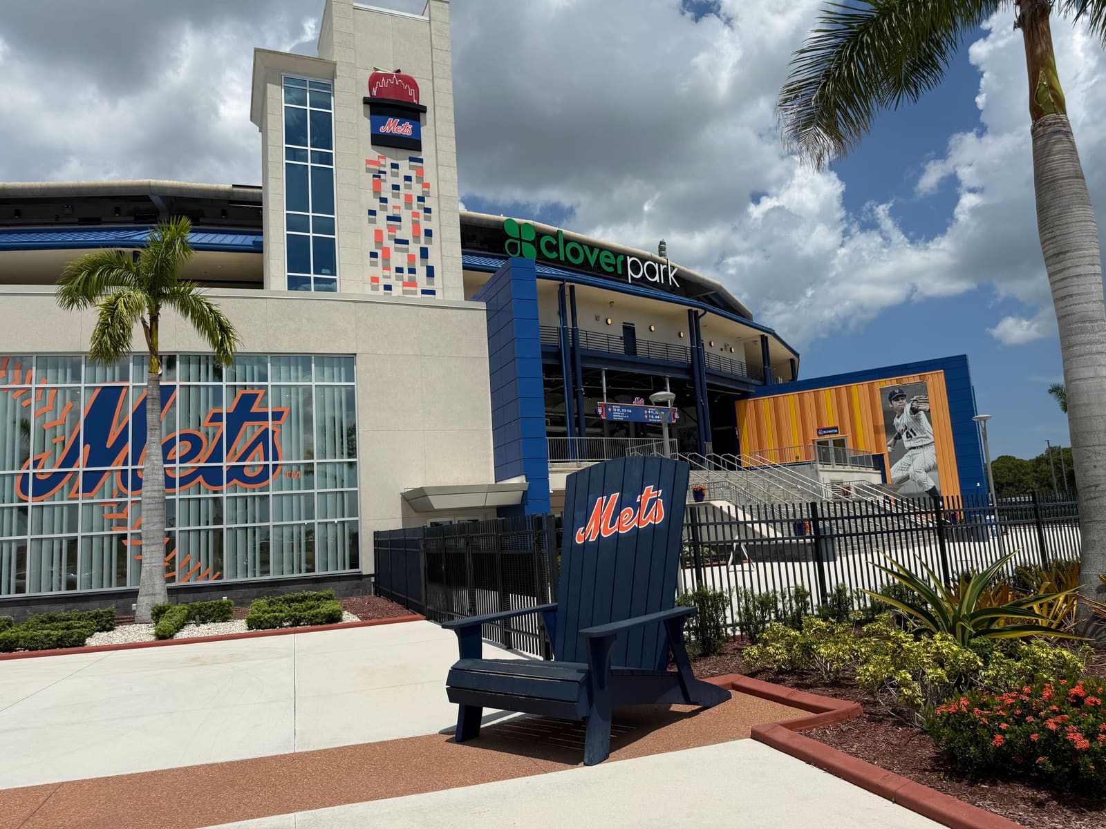 An oversized Mets-blue Adirondack chair on the Clover Park entrance plaza, with the ballpark's Mets script windows behind