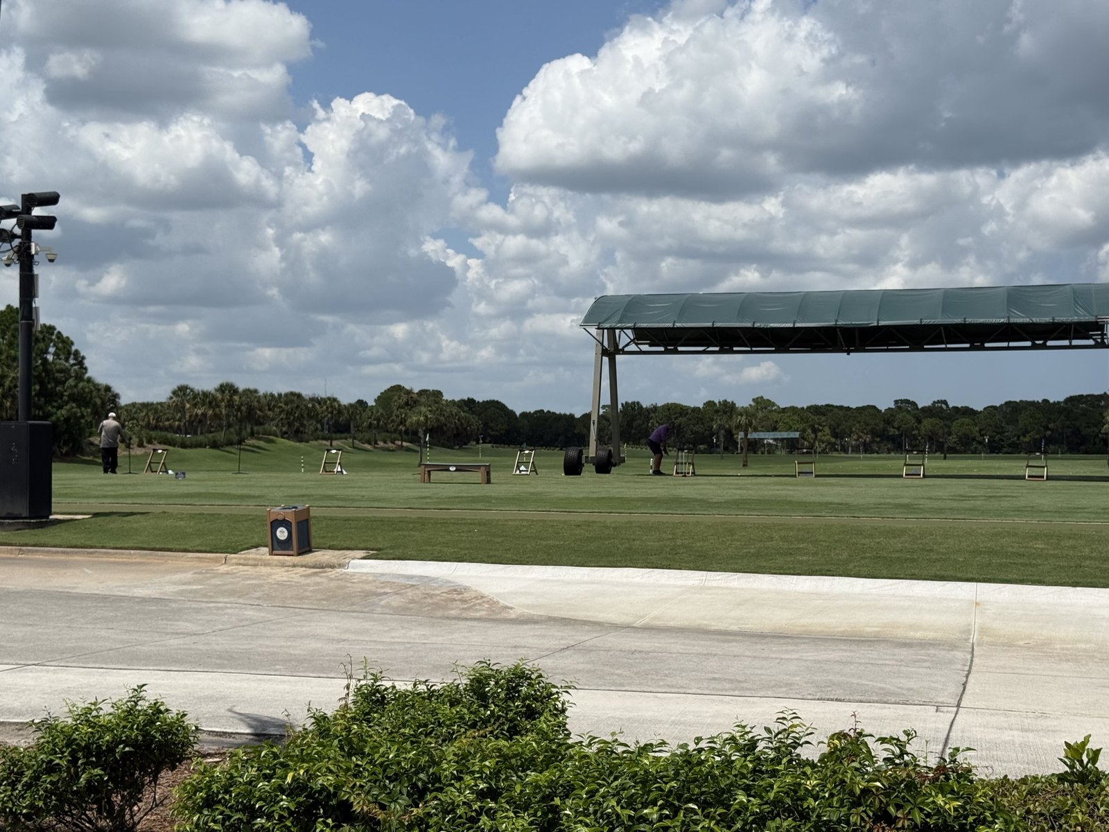 The wide grass practice range at PGA Golf Club with a covered hitting area in the distance