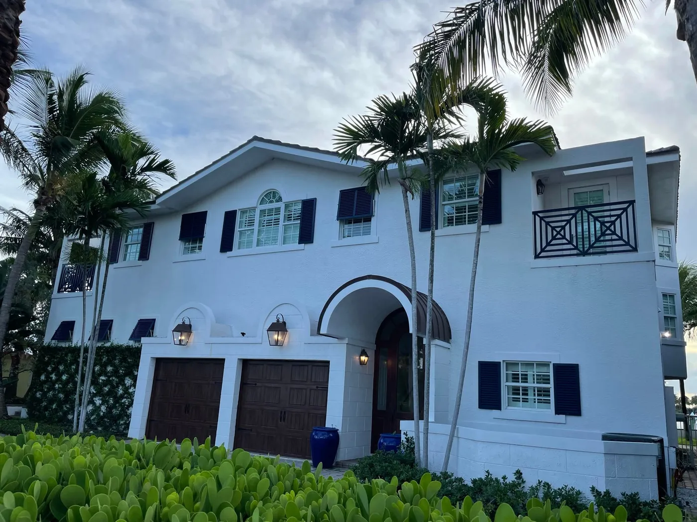 A white two-story house with dark shutters, an arched entry and a two-car garage, behind palms on Singer Island
