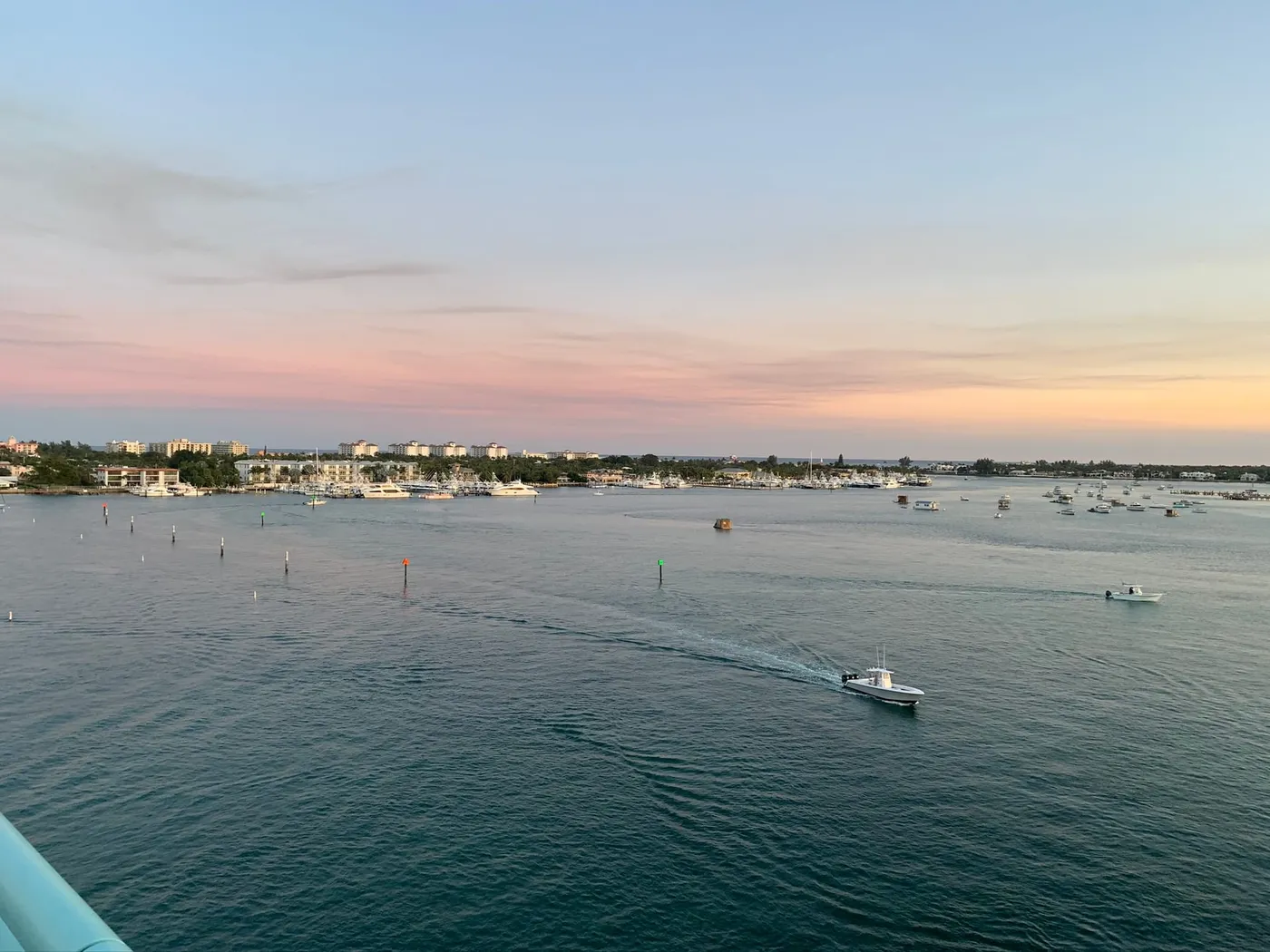 Boats crossing the lagoon at dusk toward a marina and low-rise buildings on the island, seen from the Blue Heron Bridge