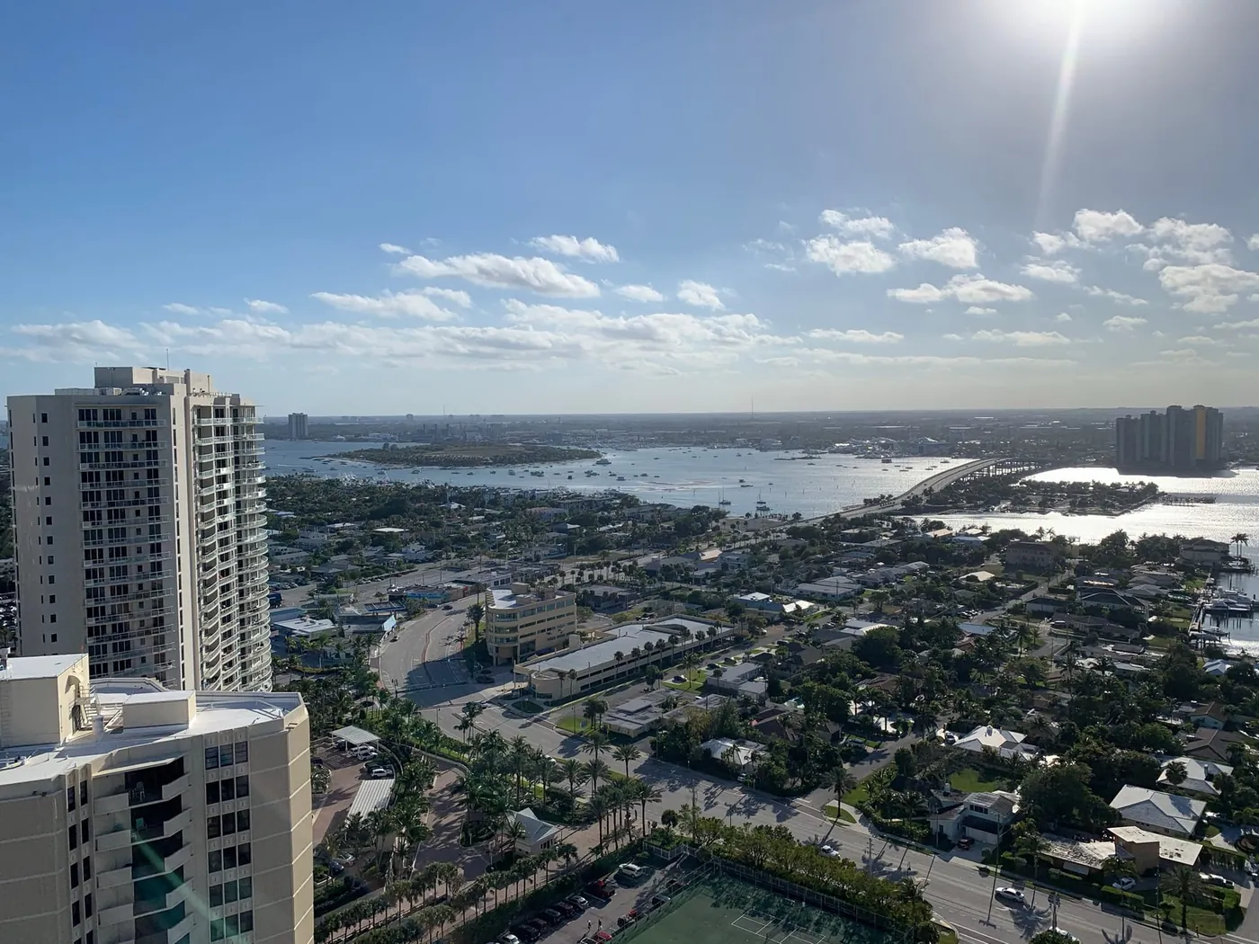 High-rise view west over Singer Island's lagoon-side streets of single-family houses and canals, with condominium towers in the foreground and the Blue Heron Bridge in the distance
