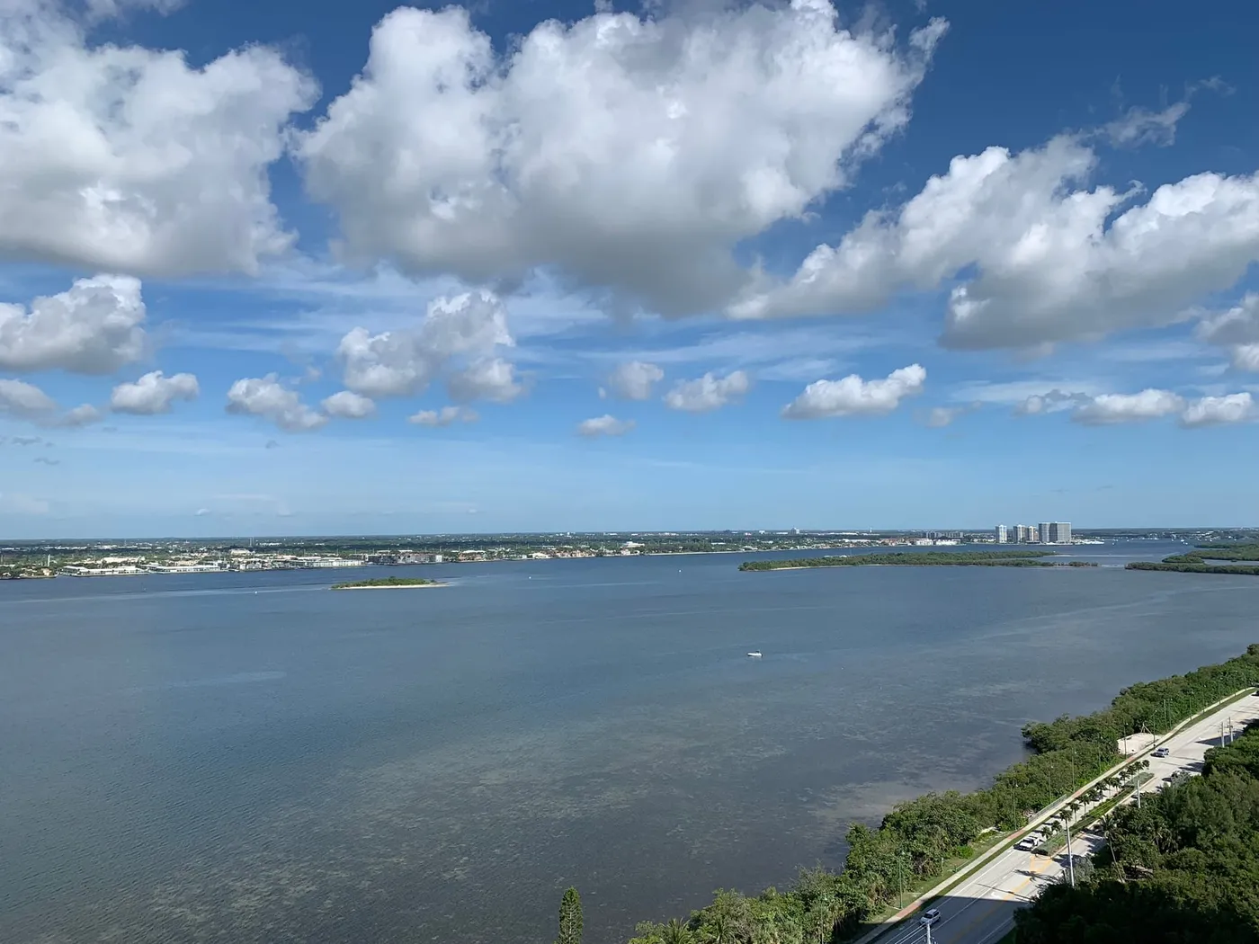 A high view north-west over the lagoon off Singer Island's north end, with small mangrove islands, a shoreline road and big cumulus clouds