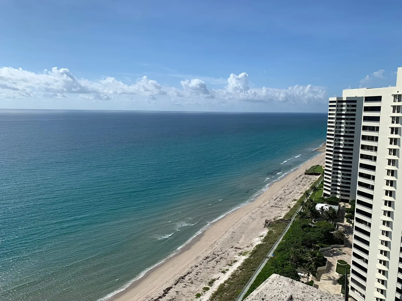 A high view south along Singer Island's beach, with turquoise water, a wide strip of sand and white condominium towers at the right