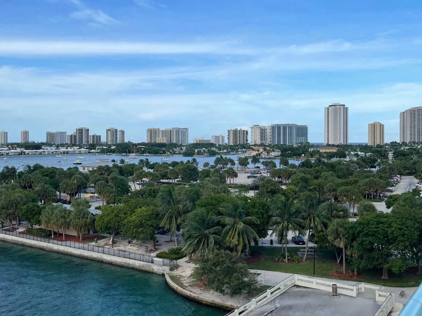 Looking down from the Blue Heron Bridge onto Phil Foster Park's seawall, trees and pavilions, with the lagoon and Singer Island's towers beyond