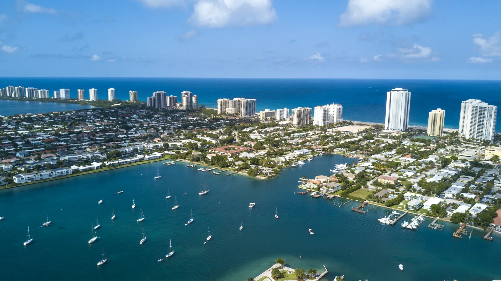 Aerial view of a coastal barrier-island community with high-rise condos, marina and anchored sailboats