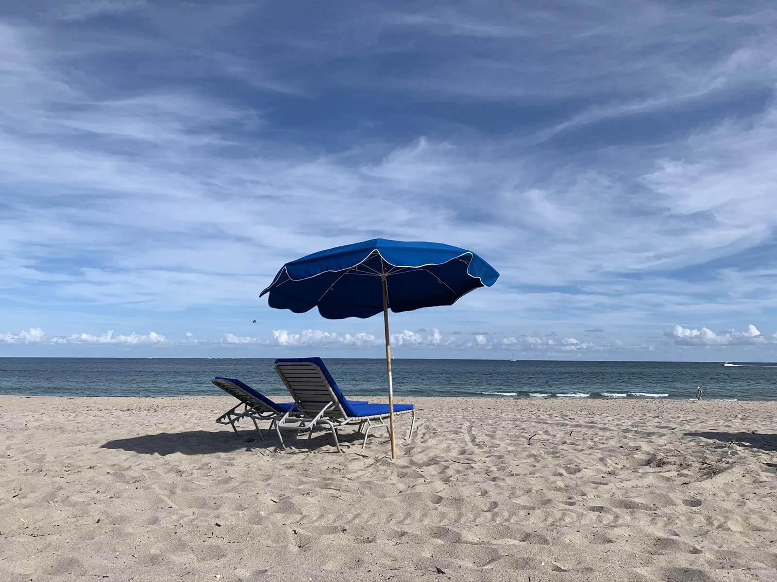 Blue beach umbrella and two striped lounge chairs on an empty sandy beach