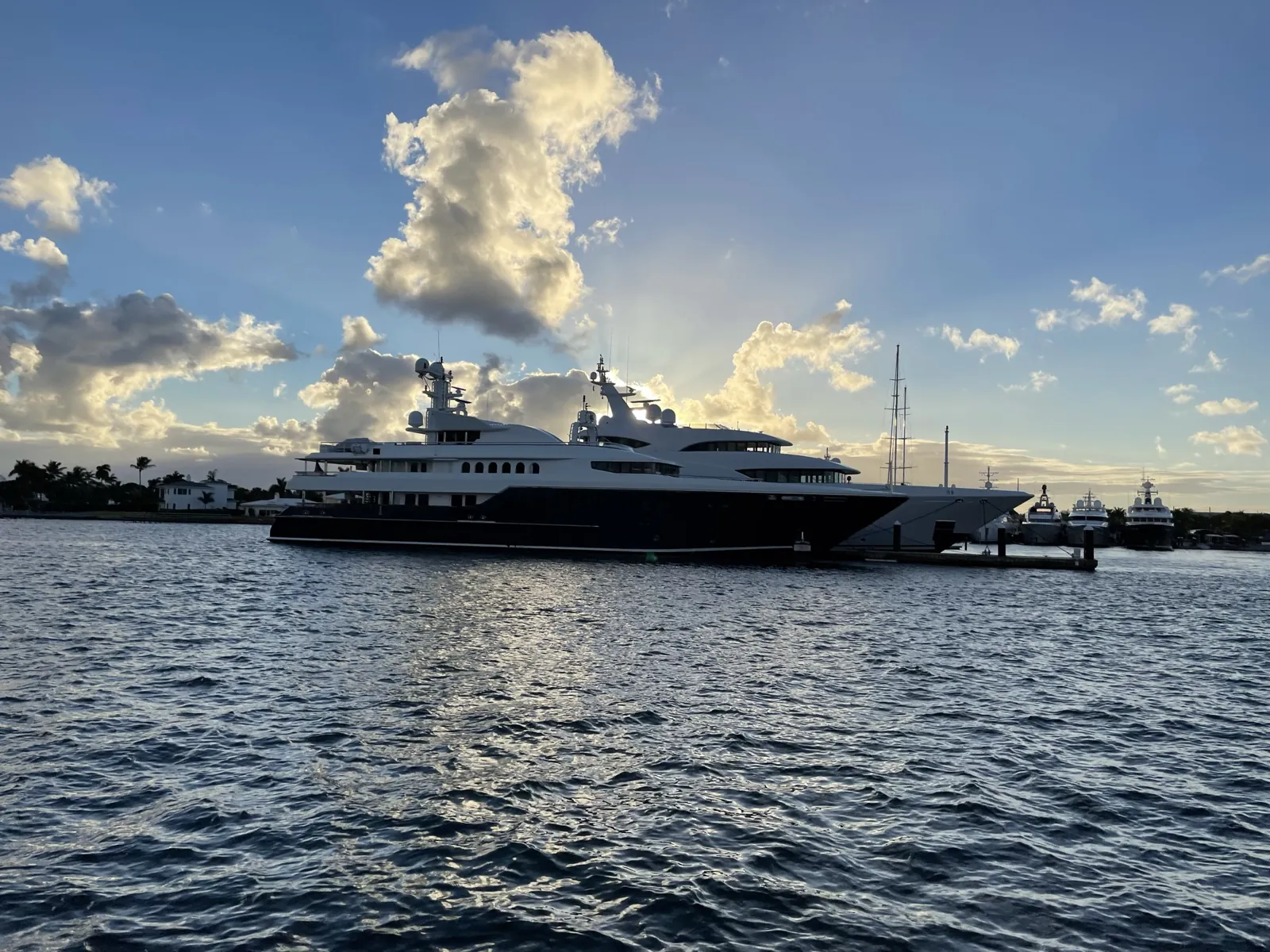 Superyachts docked at sunset with sunburst behind clouds