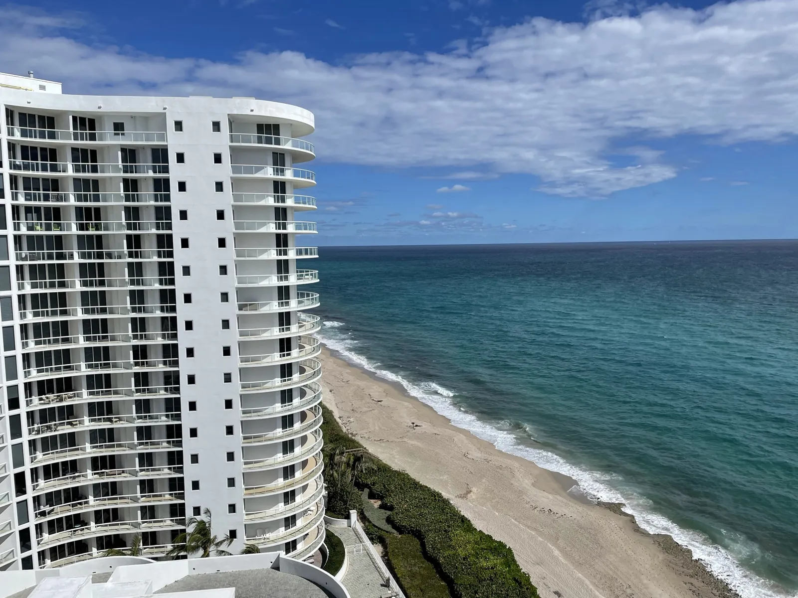 Curved white oceanfront high-rise condominium tower overlooking the Atlantic coastline and beach