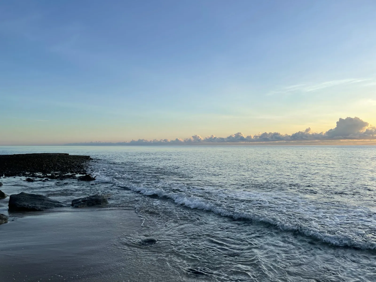 Ocean shoreline at sunrise/sunset with rocky outcrop and breaking waves