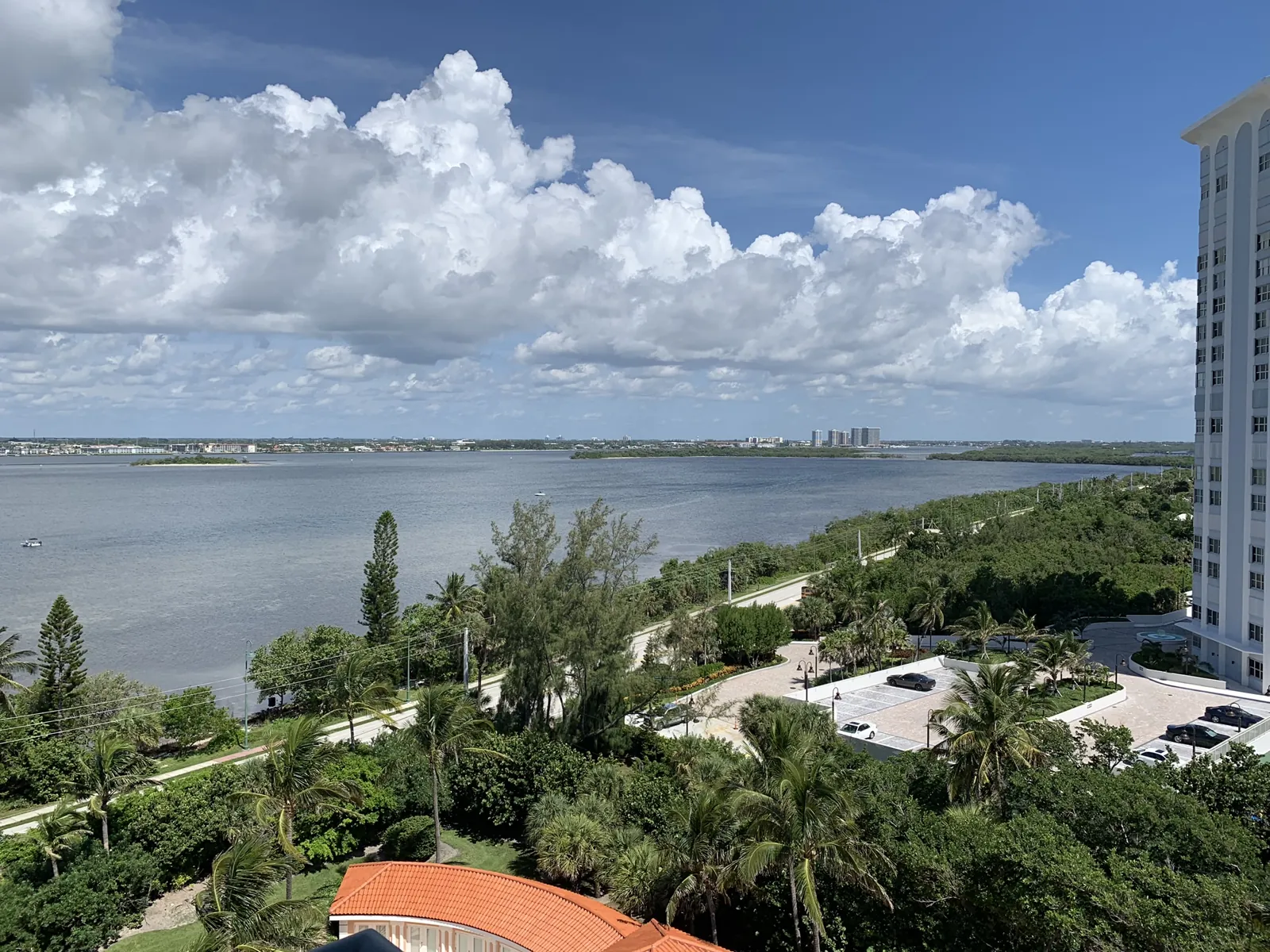 Elevated view of a wide intracoastal lagoon with mangrove shoreline, coastal road, and lush tropical landscaping beneath dramatic cumulus clouds