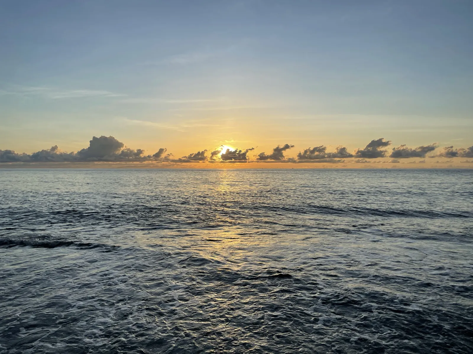 Sunrise over the open ocean with scattered low clouds on the horizon