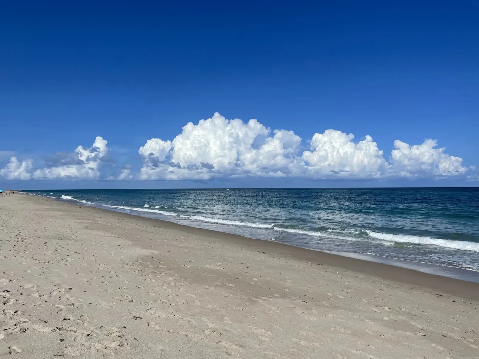Empty Atlantic beach with rolling surf and towering cumulus clouds under deep blue sky