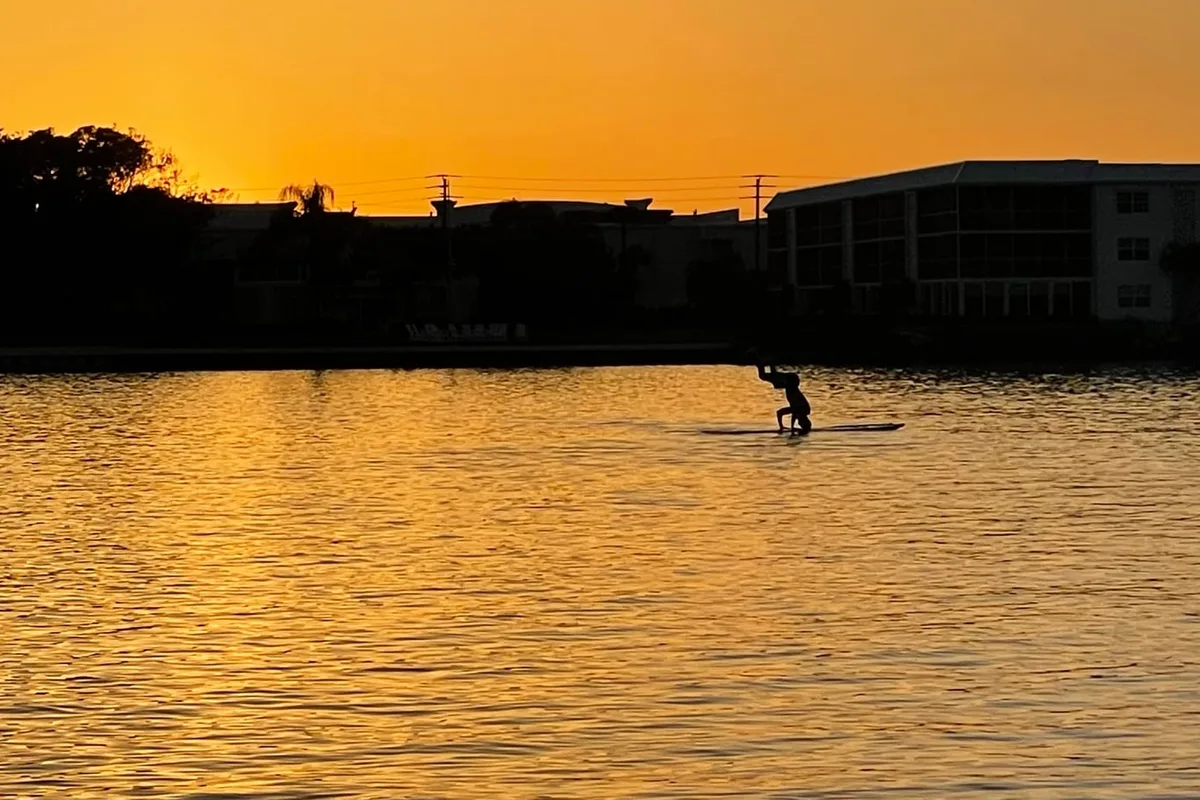 A paddleboarder at dusk on calm golden water near Tequesta